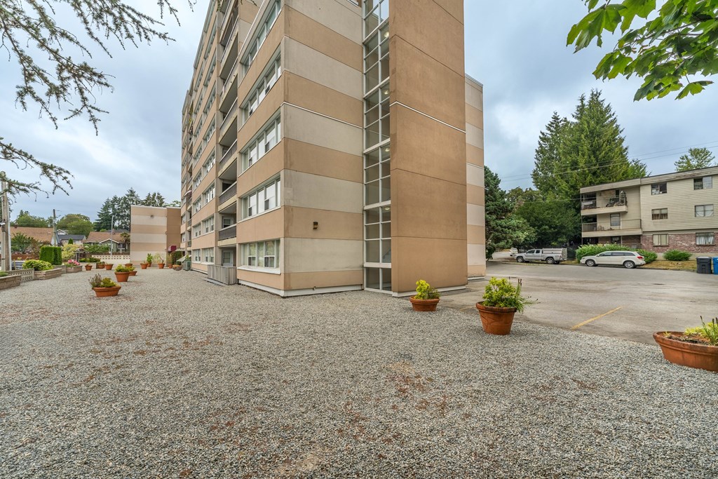 A gravel courtyard in front of a tan building with a tree in the background.