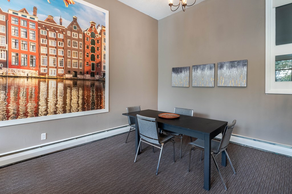 A room with a table and chairs and a picture of a canal house on the wall.