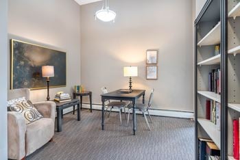 A living room with a grey couch, a table with a lamp, a chair and a bookshelf.