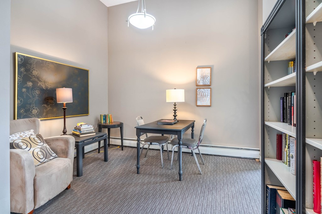 A living room with a grey couch, a table with a lamp, a chair and a bookshelf.