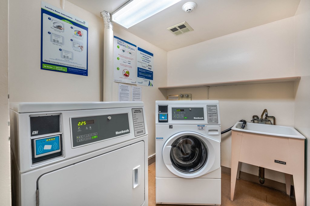 A washing machine and dryer are in a small room with instructions on the wall.