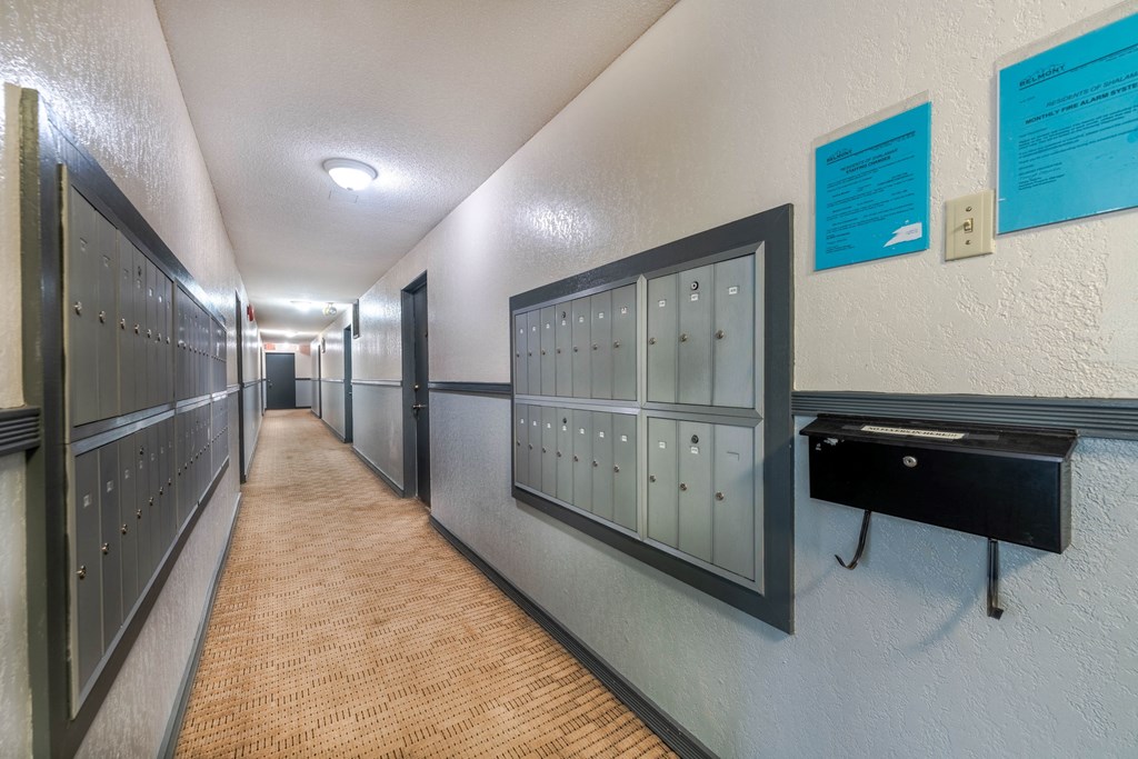 A long hallway with a series of lockers on the side and a black trash can.