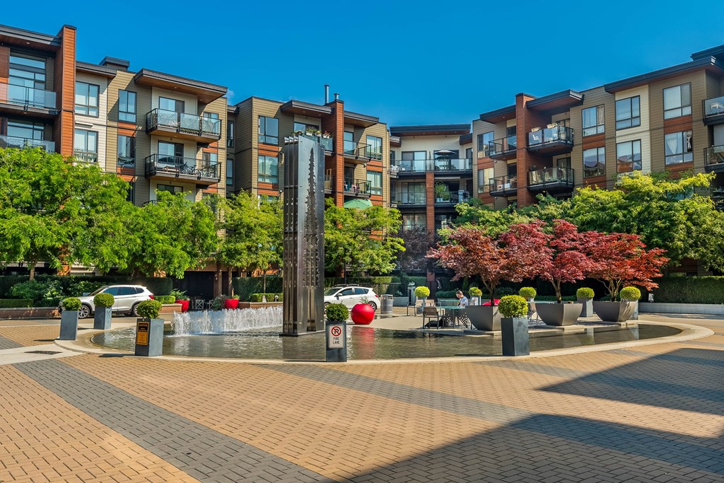 A fountain in the middle of a brick square with apartment buildings in the background.