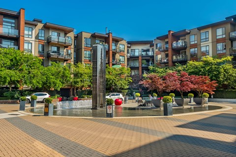 A fountain in the middle of a brick square with apartment buildings in the background.
