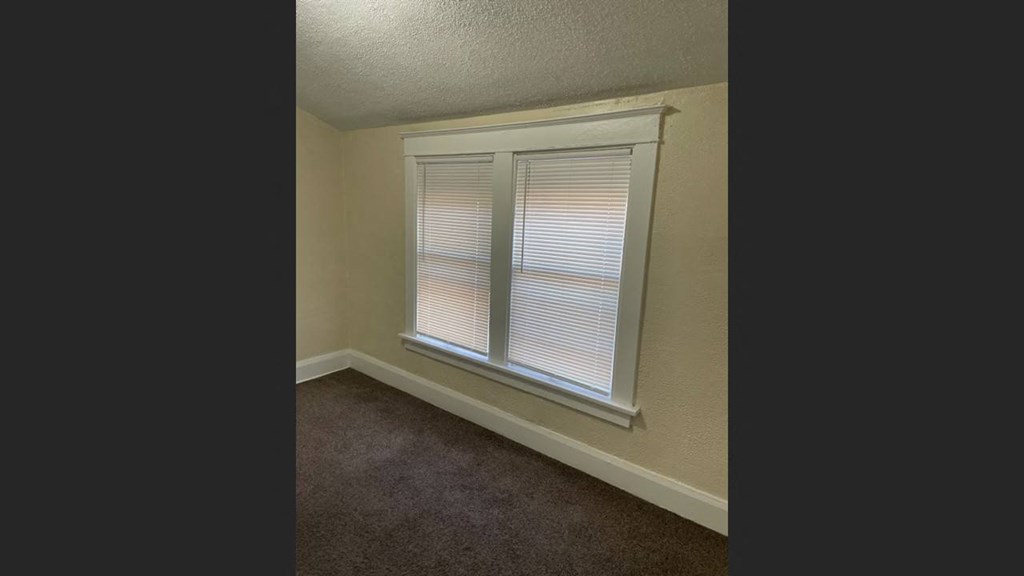 the bedroom has a large window and a carpet
