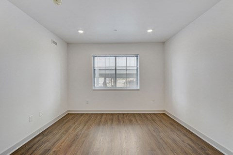 a bedroom with white walls and wood floors and a window