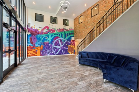 A brightly lit hallway with a blue couch and a colorful mural on the wall.