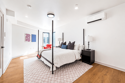A bedroom with a white bed and a black speaker on a table.