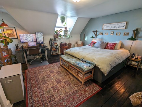 A bedroom with a bed, a rug, and a framed picture on the wall.