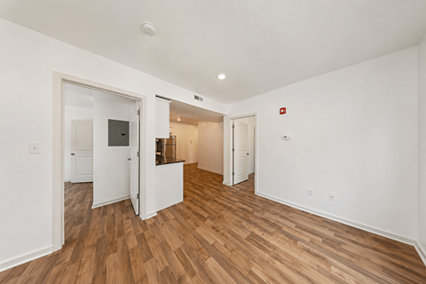 A room with white walls and wooden flooring with a doorway leading to another room.