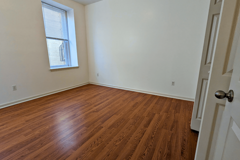 an empty bedroom with wood floors and a window