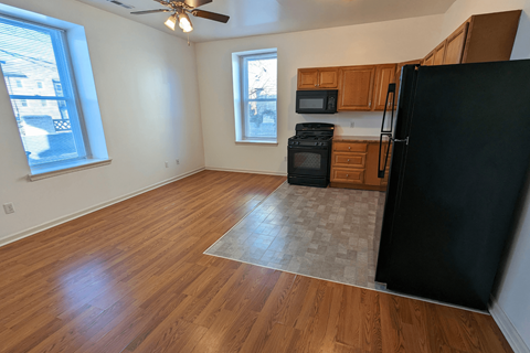 an empty living room and kitchen with wood floors and a black refrigerator