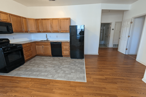 an empty kitchen with wood floors and a black refrigerator
