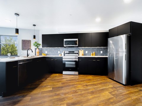 A modern kitchen with black cabinets and a wooden floor.