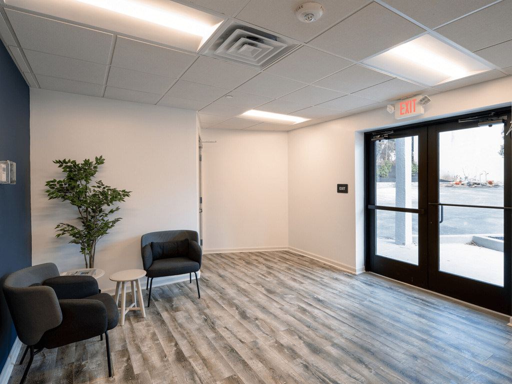 an empty room with chairs and a plant in front of a glass door