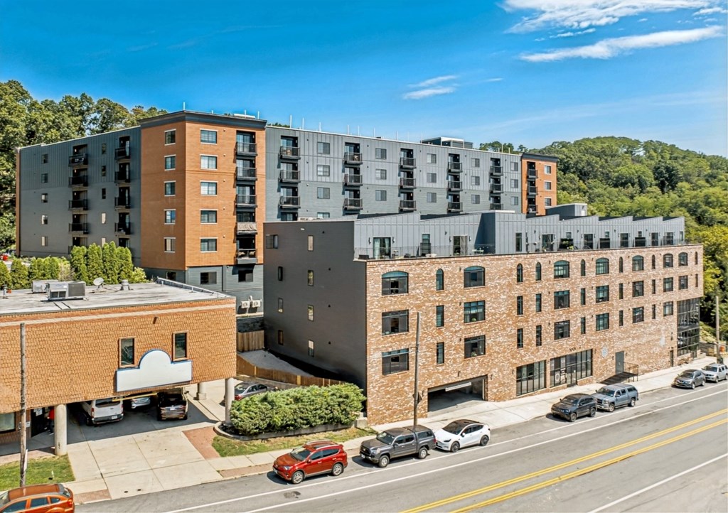 A street view of a residential area with cars parked on the side of the road and multi-story buildings in the background.