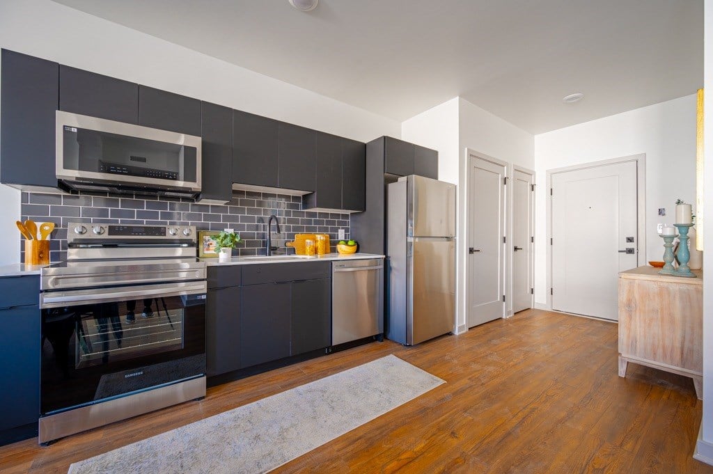 A modern kitchen with dark grey cabinets and a wooden floor.