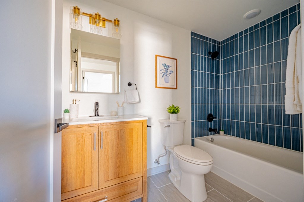 A bathroom with a white toilet, wooden medicine cabinet, and blue tiled wall.