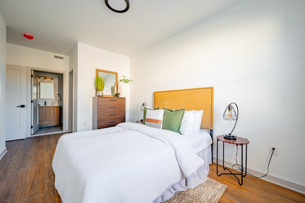 A bedroom with a bed, nightstand, and a plant on the dresser.