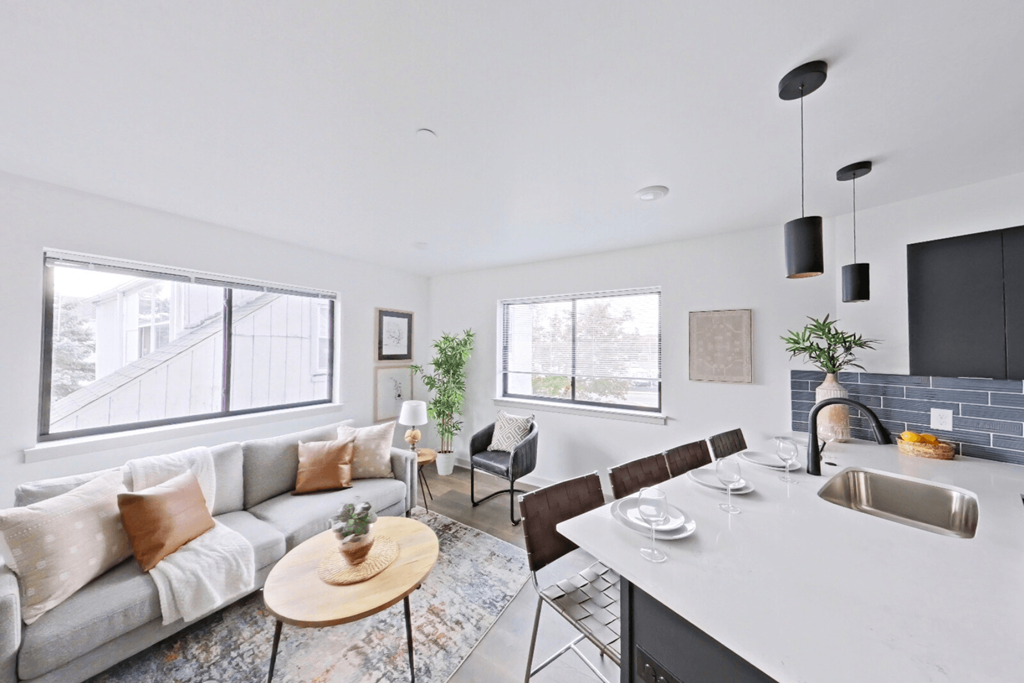 A modern living room with a grey sofa, a wooden coffee table, and a kitchen area with a sink.