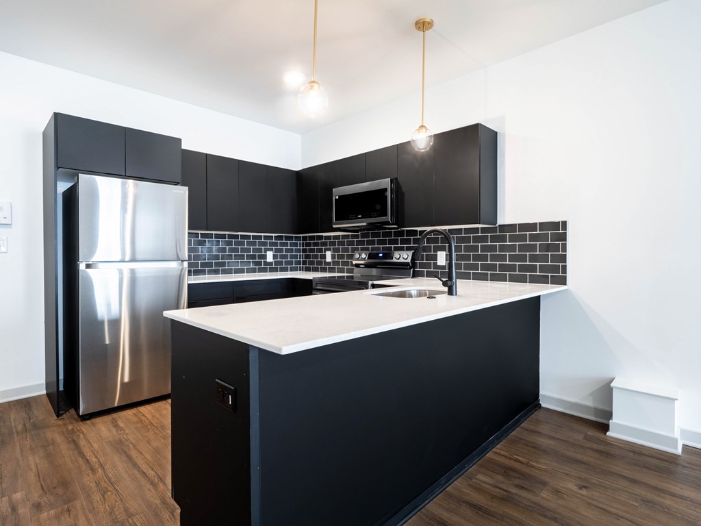 A modern kitchen with black cabinets and a stainless steel refrigerator.
