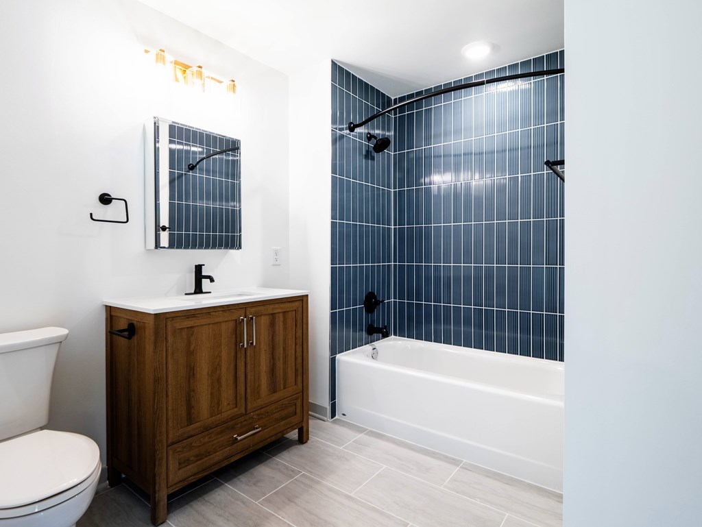 A bathroom with a white toilet, a wooden cabinet, and a blue tiled shower.
