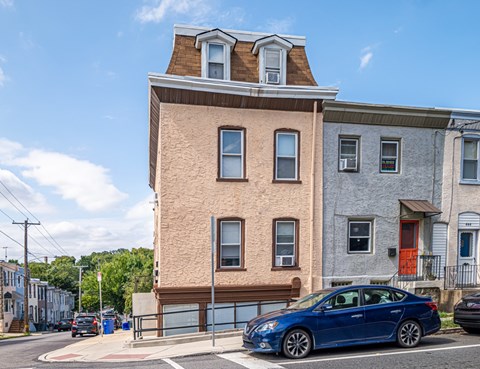 A blue car is parked in front of a tan building.