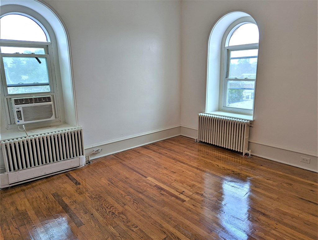an empty room with wooden floors and two windows