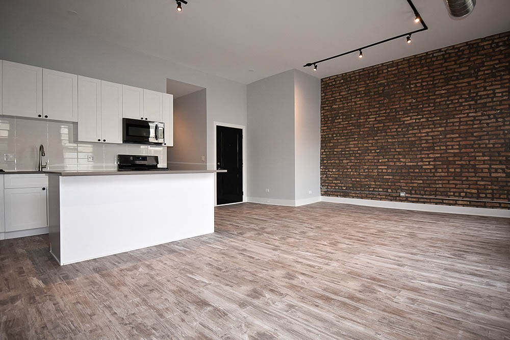an empty living room with a kitchen and a brick wall