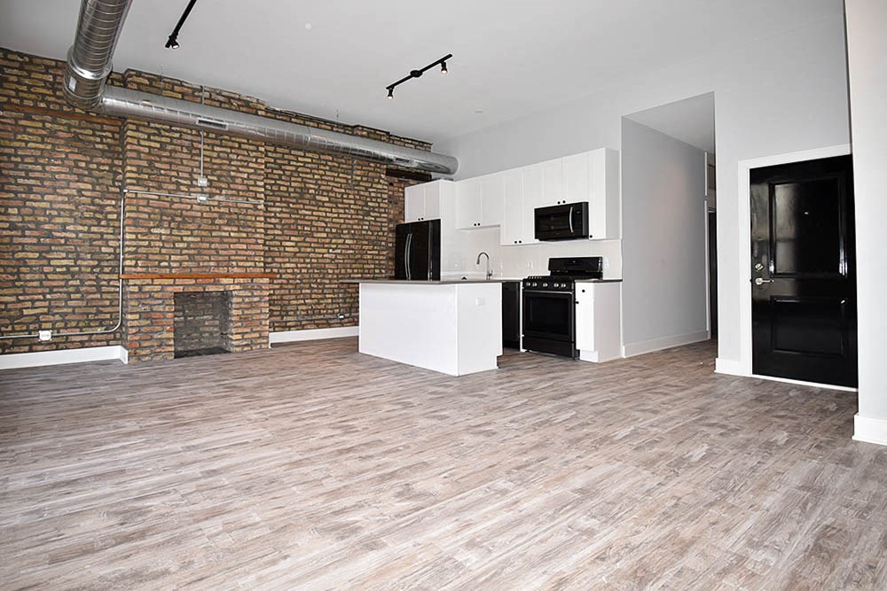 an empty living room with a brick wall and a kitchen
