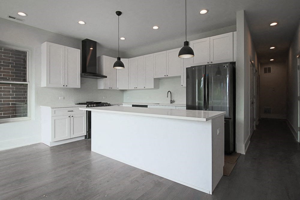 a white kitchen with a large island and a stainless steel refrigerator