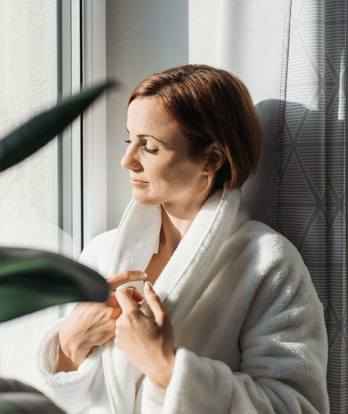 woman in a bathrobe looking out the window on a sunny day