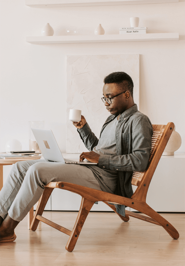 a man sitting in a chair with a laptop and a cup of coffee