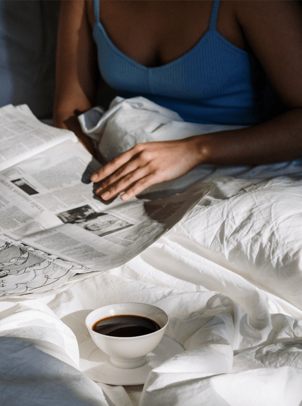 a woman sitting in bed with a cup of coffee and a newspaper
