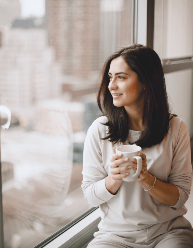 woman sitting on a window sill holding a cup of coffee