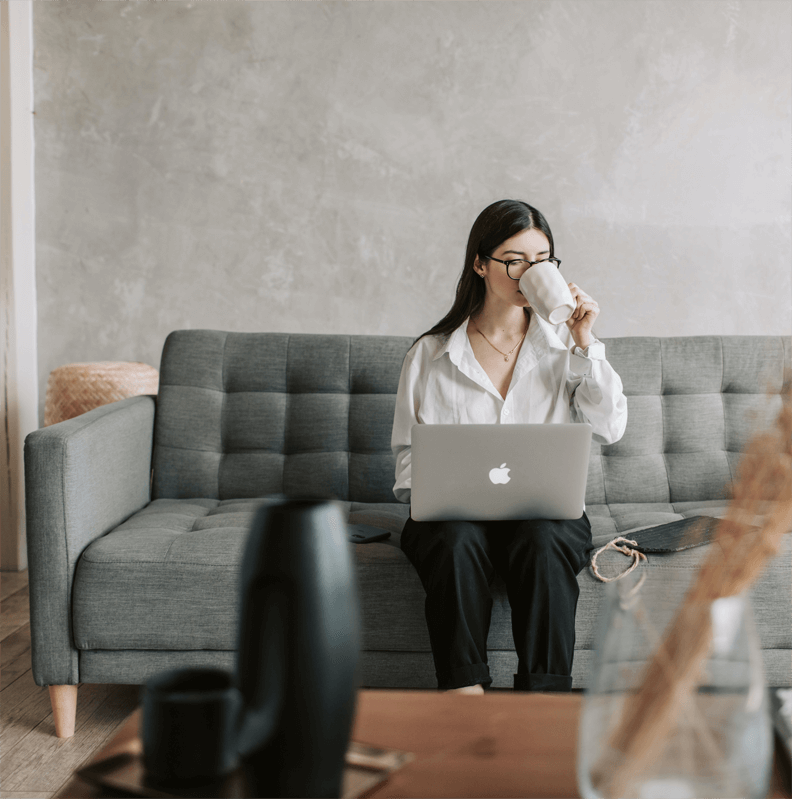 a woman sitting on a couch drinking coffee and working on her laptop
