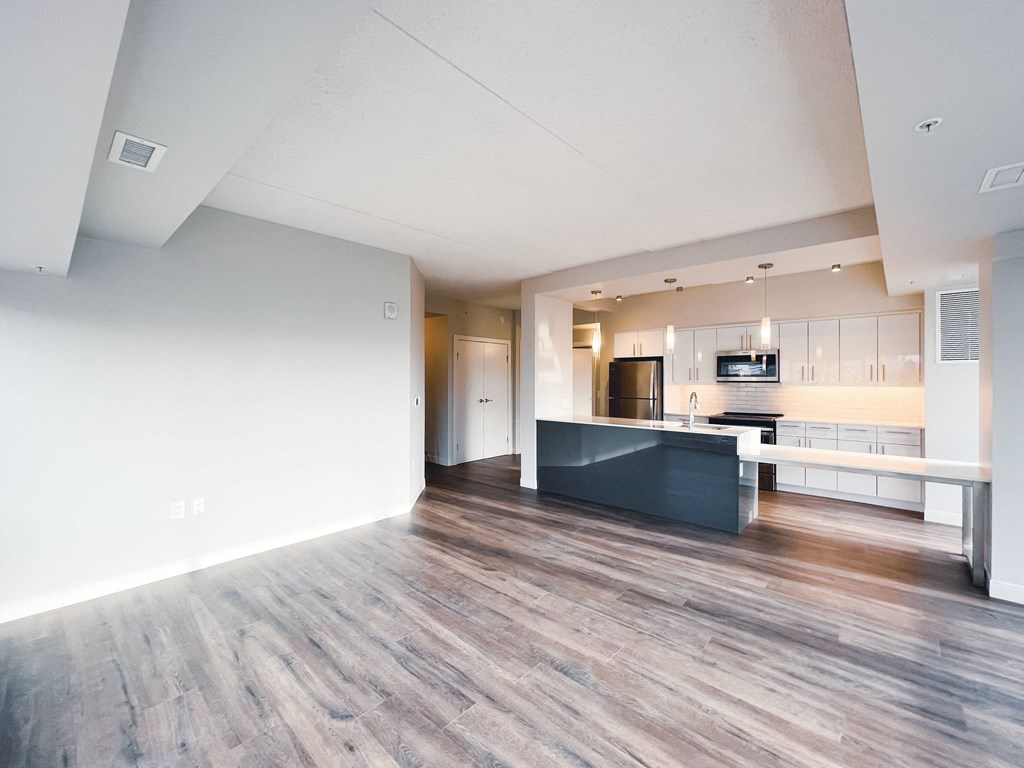 an empty living room with a kitchen in the background