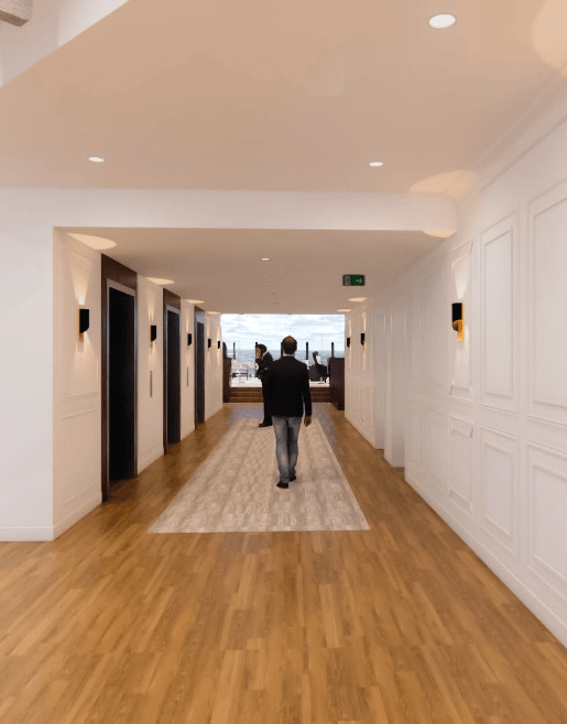 a man walking down a long hallway with white walls and wood floors