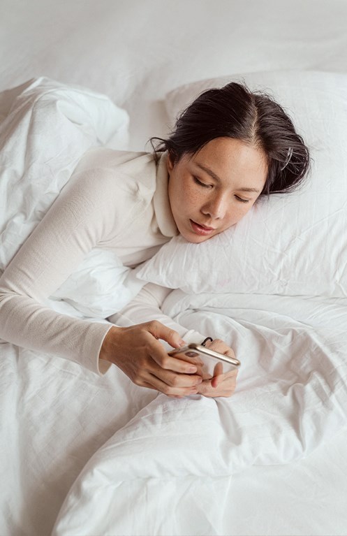 a woman laying in bed looking at her cell phone