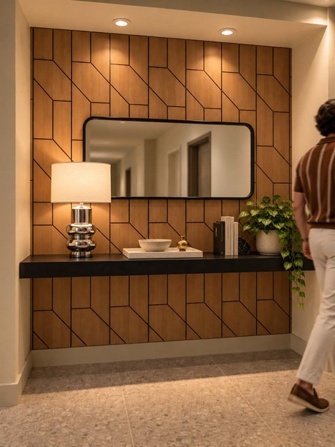 A man is walking past a wooden wall with a mirror and a lamp on it.