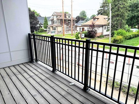 A black metal railing on a wooden deck overlooks a residential street.