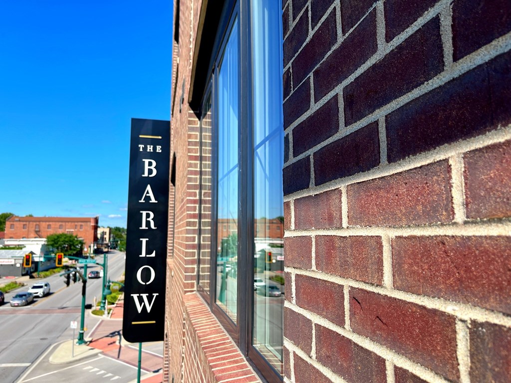 A sign that says "The Barlow" is mounted on a brick wall.