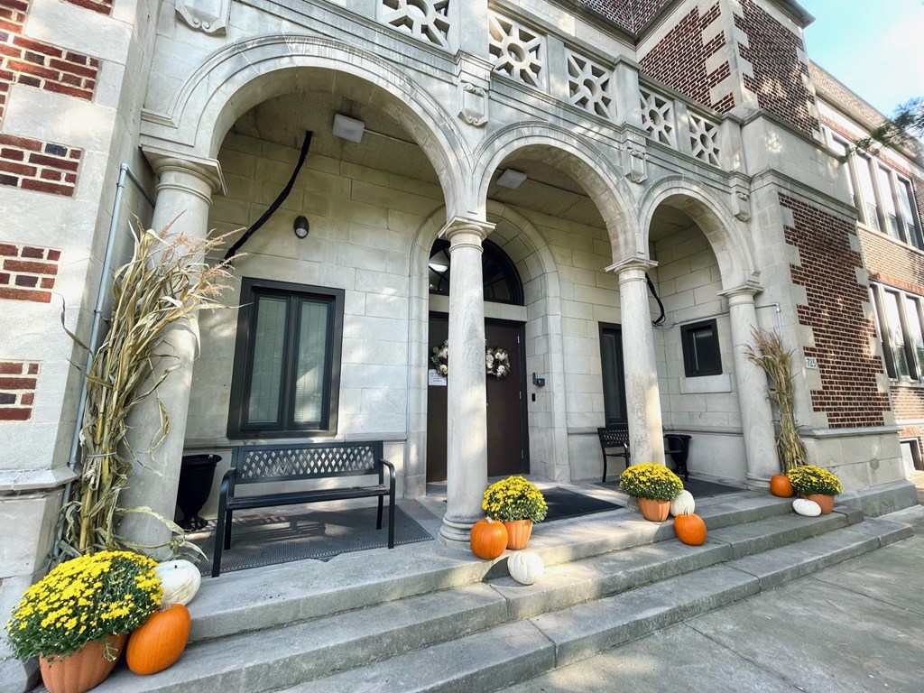 A building entrance with a bench and pumpkins on the steps.
