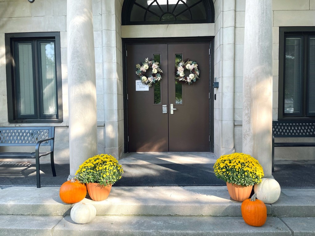 A brown door with a flower wreath and two pumpkins in front of it.