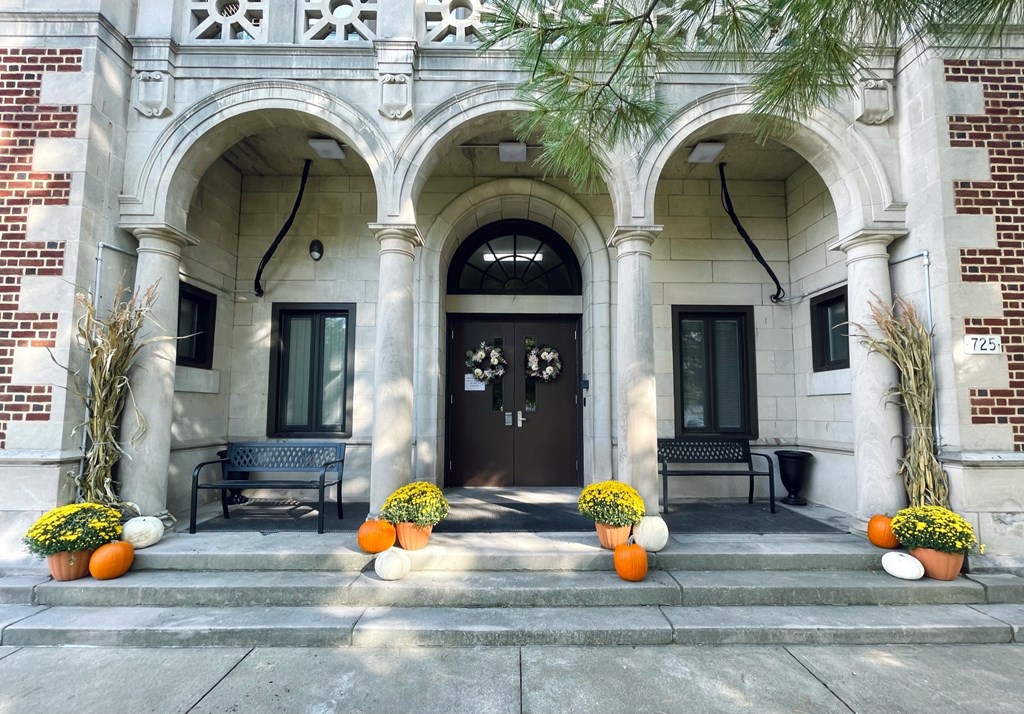 A building with a black door and windows is decorated with pumpkins and plants.