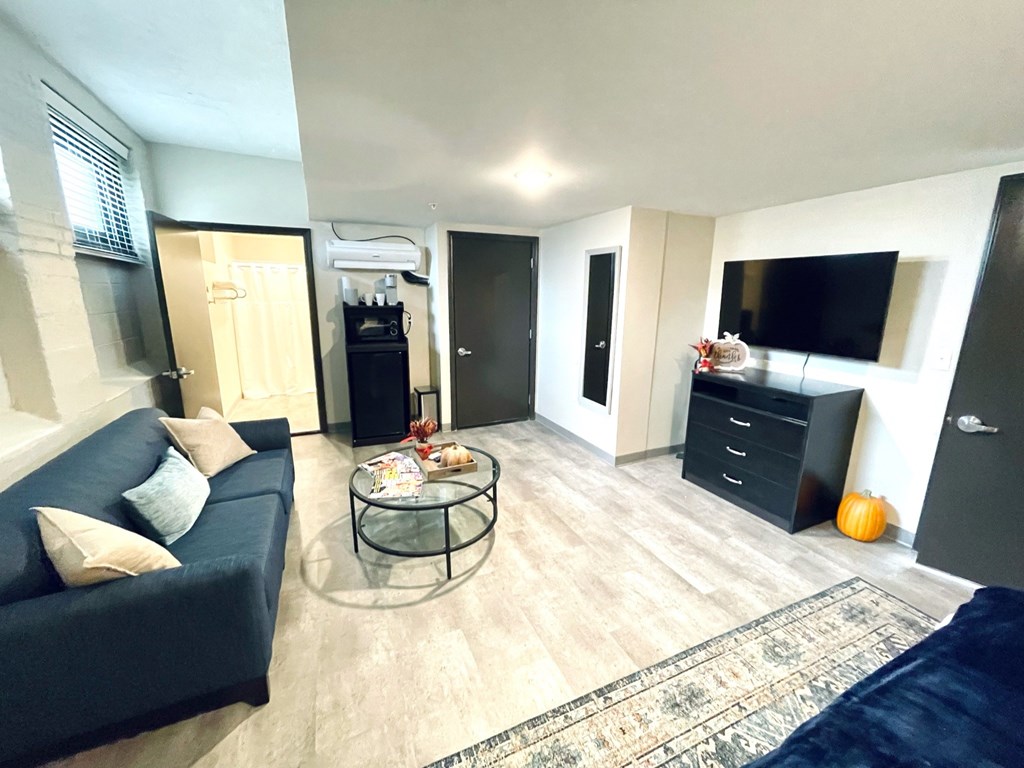 A living room with a blue couch, a glass coffee table, and a TV mounted on the wall.