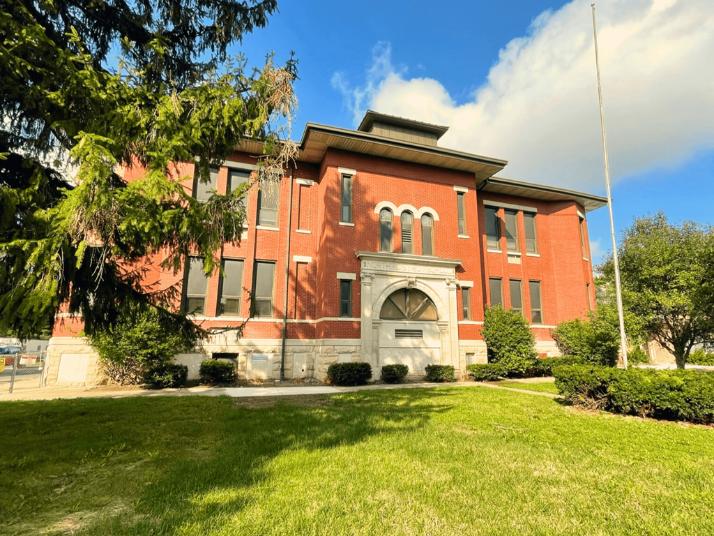 A red building with a white arched entrance sits on a green lawn.