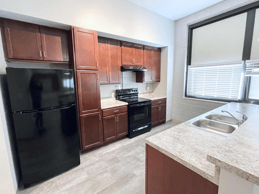 A kitchen with brown cabinets and a black refrigerator.