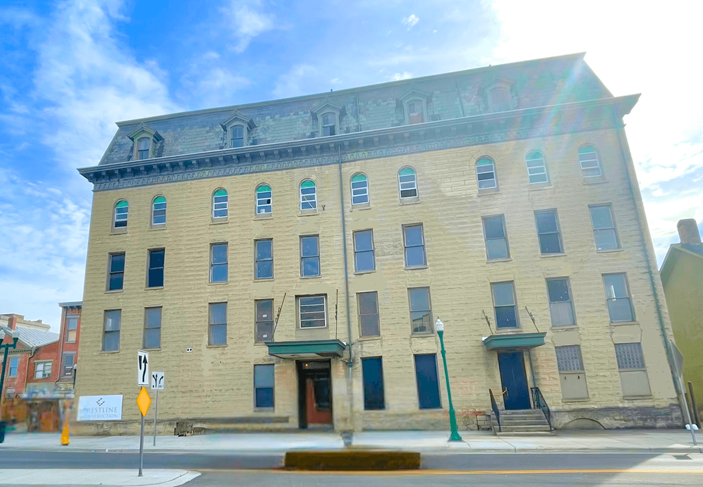 A large, old building with a green awning sits on a street corner.