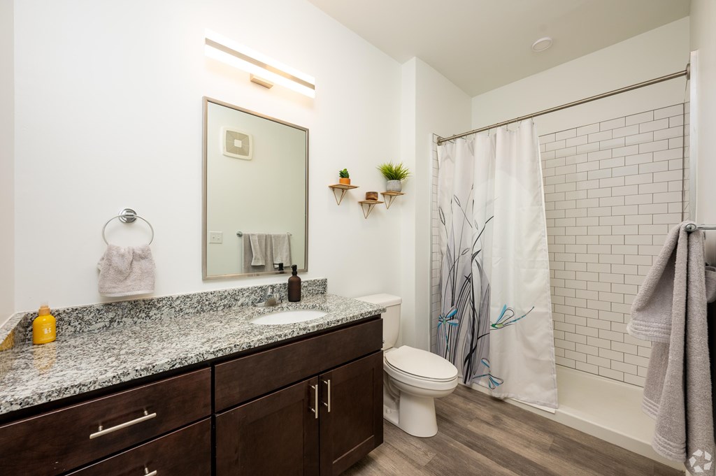 A bathroom with a white toilet, a sink with a marble countertop, and a shower with a white curtain.